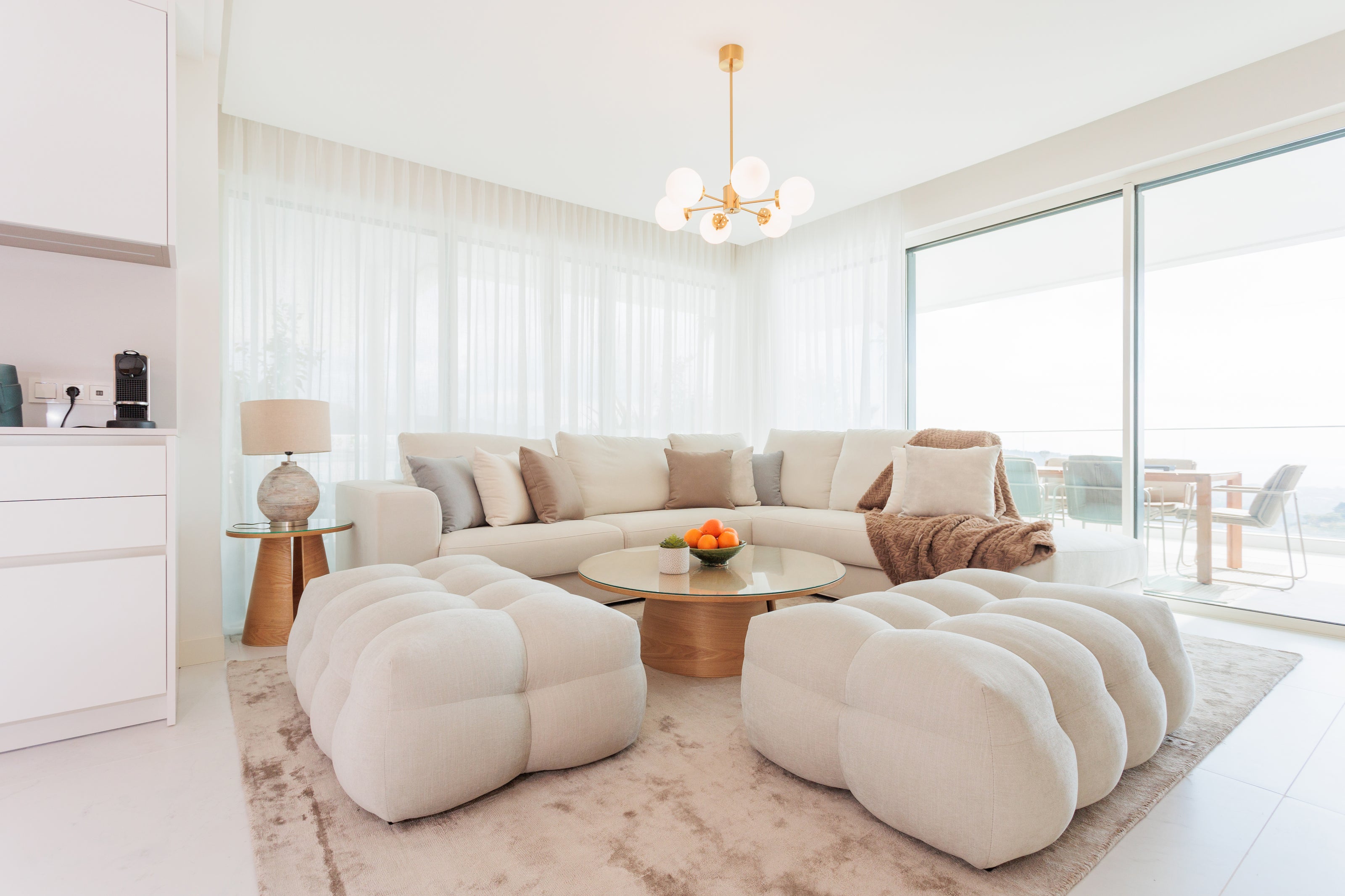 luxury comfortable interior design for living room with cream sofa, soft ottomans, elegant rug, pillows, coffee tables available in brisas del mar estepona real estate, marbella, malaga, bel air, costa del sol.