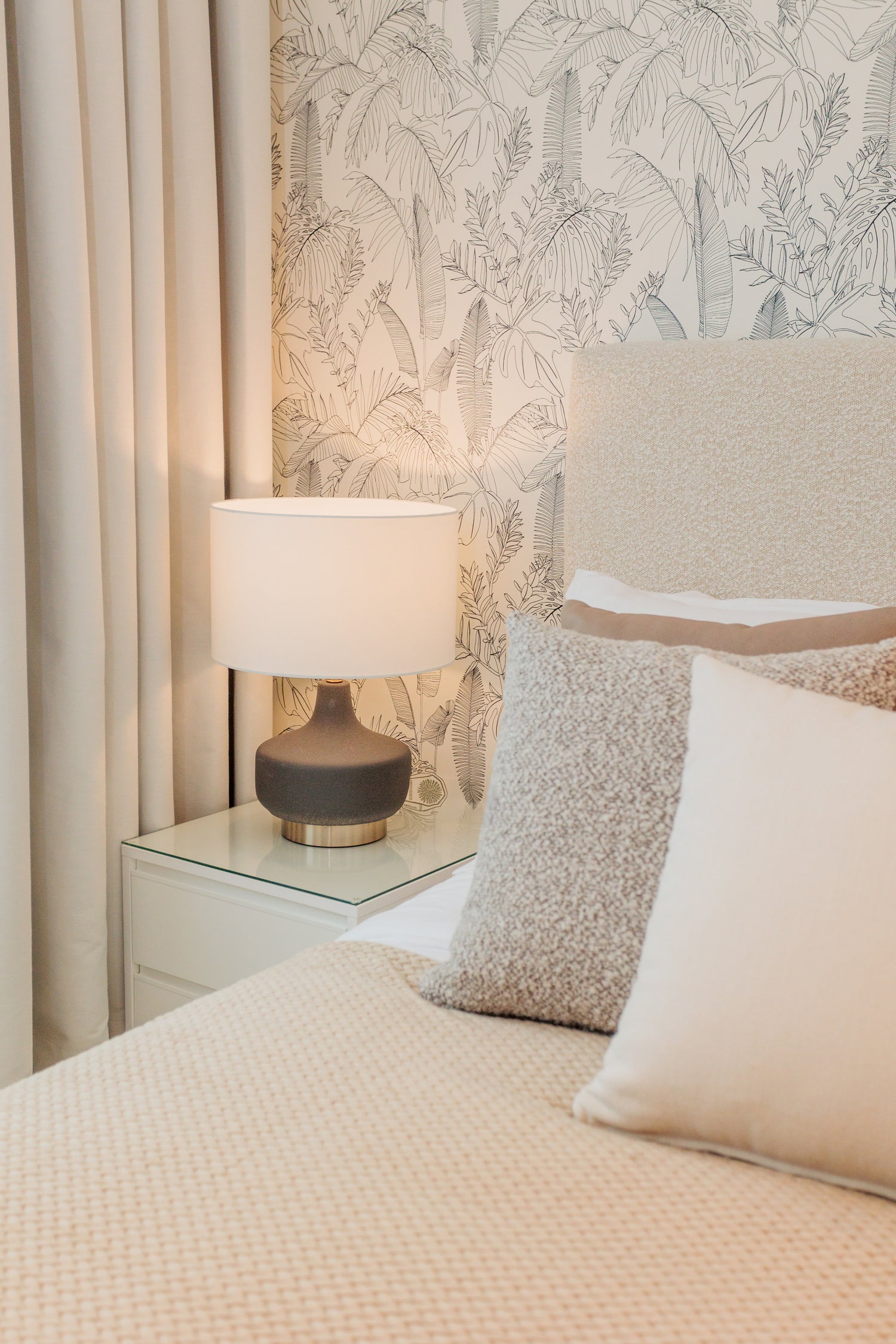 luxury interior design for bedroom, minimalist brown beige colors, with brown and gold table lamp, wallpaper with leaves design, bed with beige headboard and cream pillows available in benalmadena, marbella, malaga, costa del sol.