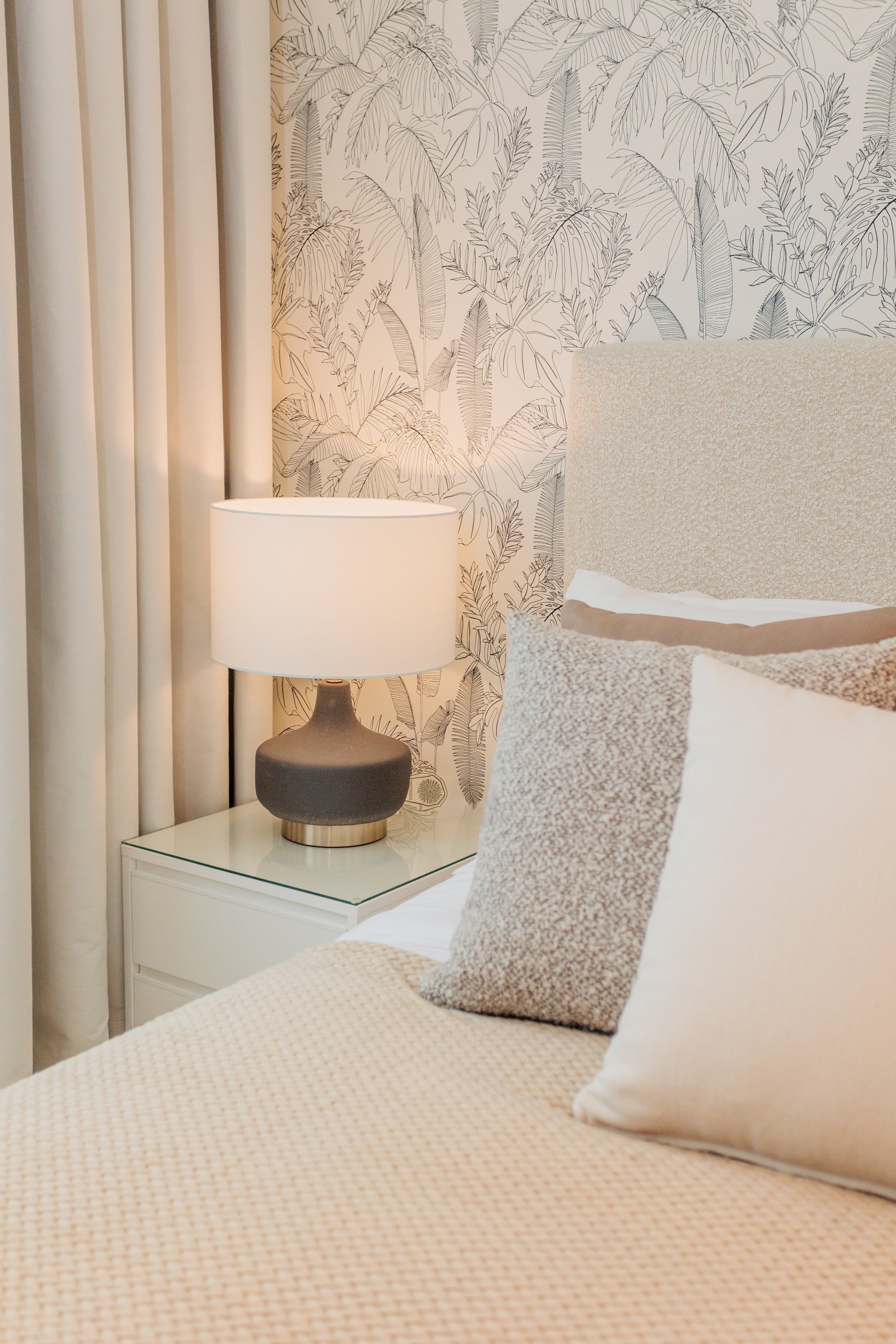 luxury interior design for bedroom, minimalist brown beige colors, with brown and gold table lamp, wallpaper with leaves design, bed with beige headboard and cream pillows available in benalmadena, marbella, malaga, costa del sol.
