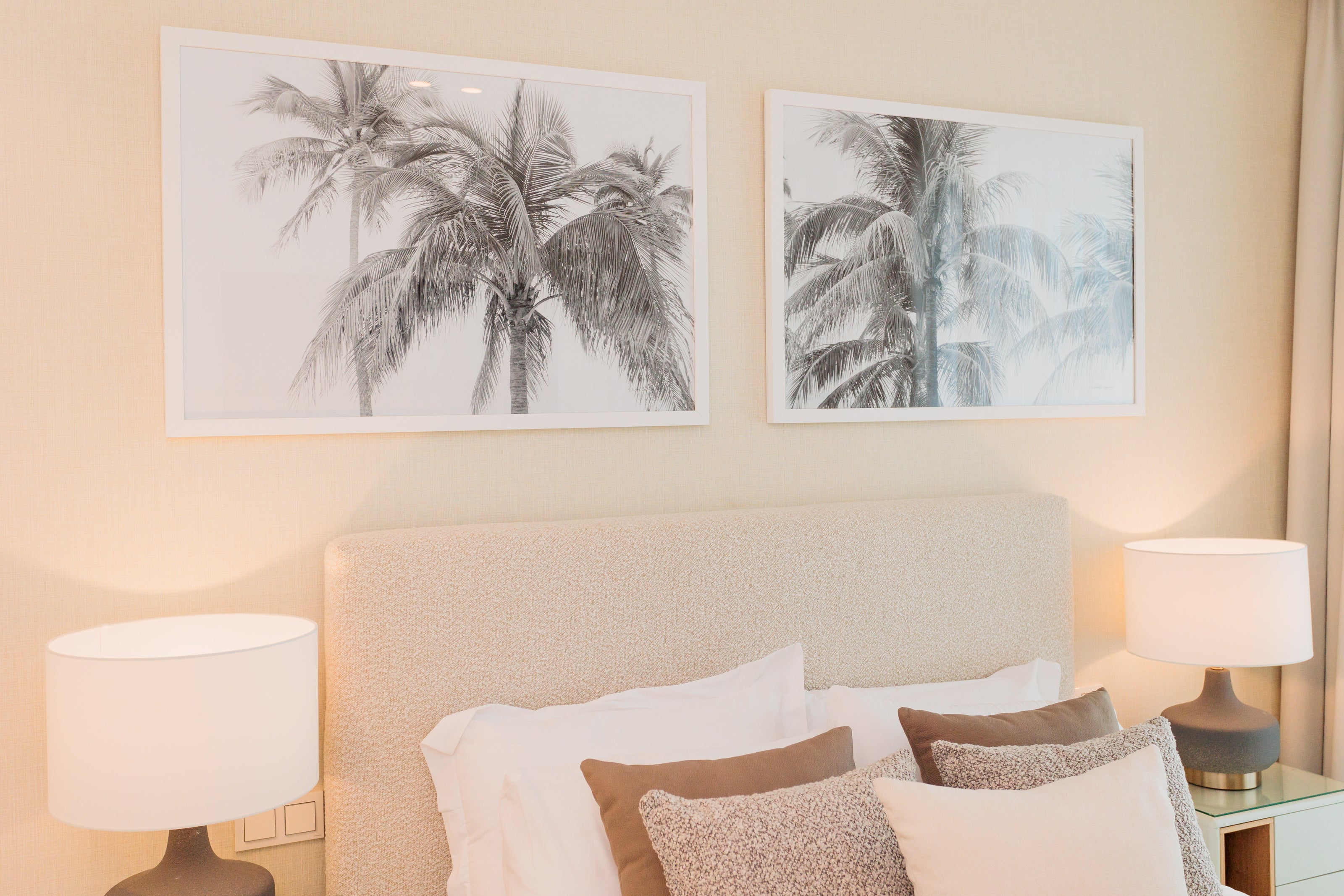 luxury interior design for bedroom with beige and cream tones, femenine, headboard with texture cream,, brown and cream pillows, greyish brown table lamps, palm tree artworks available in benalmadena, marbella, malaga, costa del sol.