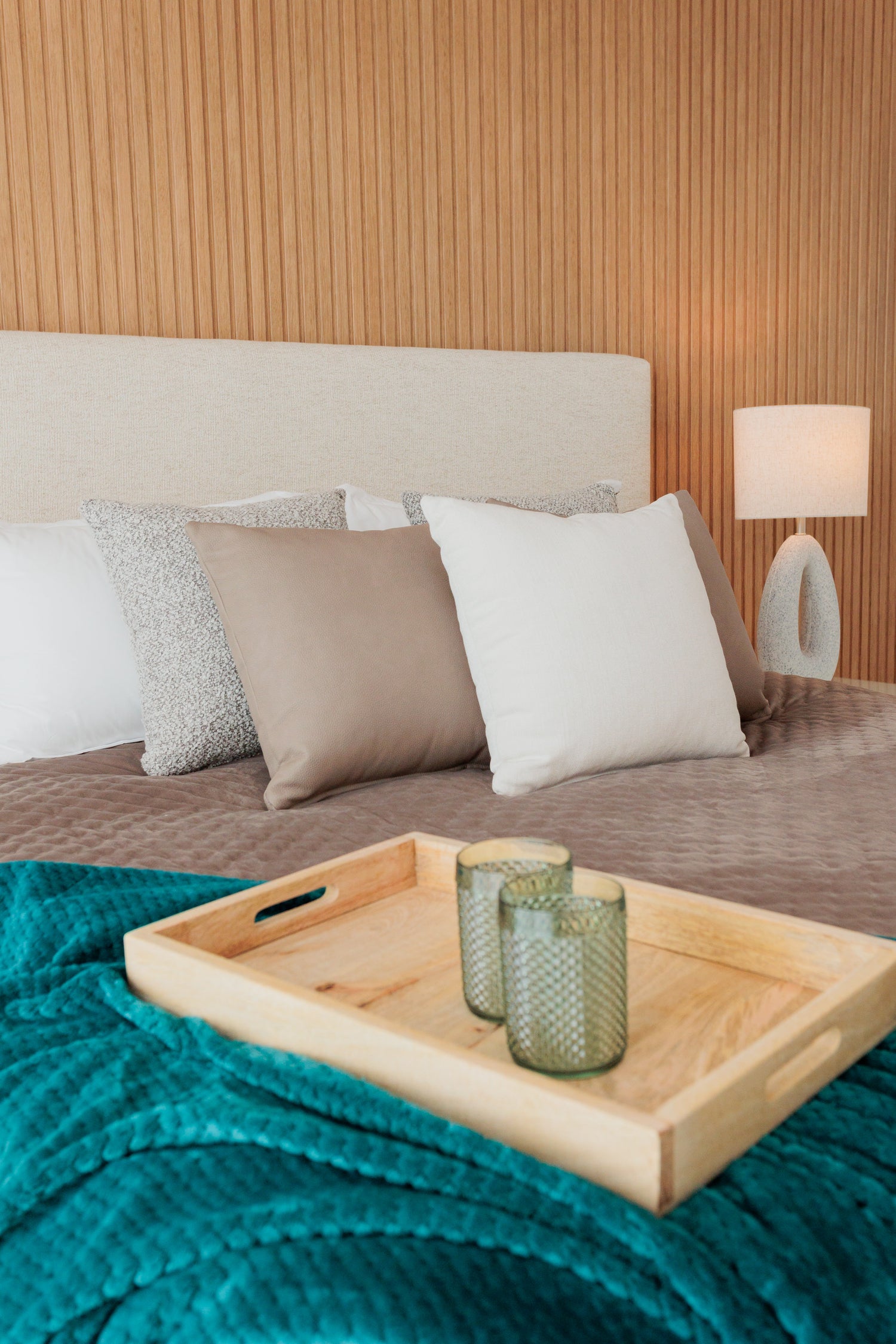 interior design for bedroom with wooden walls, cream color headboard, brown bed, green accents, wooden serving tray, oval table lamp in bel air, marbella, malaga, costa del sol.