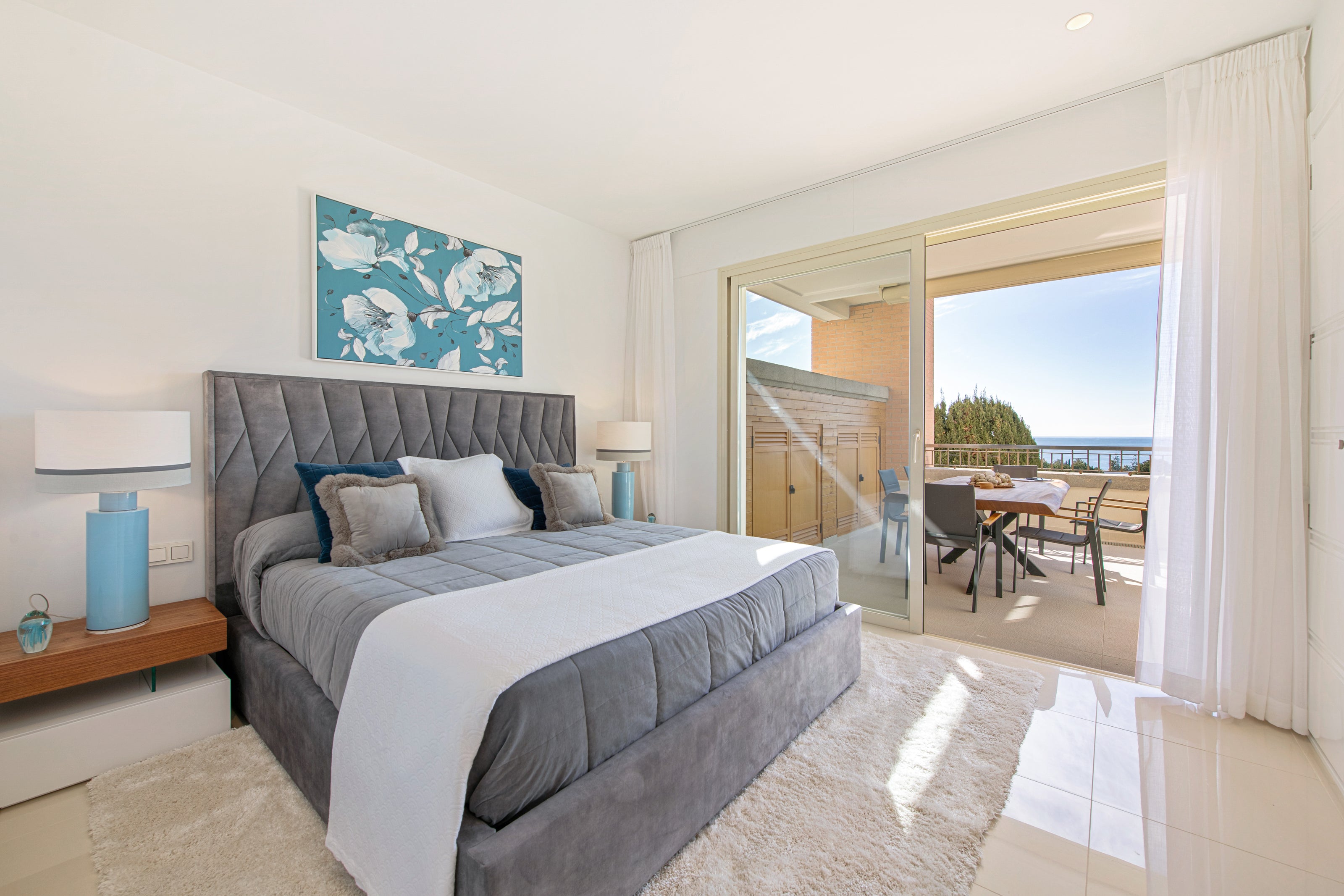 grey bed with stylish headboard with triangular shapes. bedside table, blue lamp, blue painting and voiles in a bedroom. available in el higueron, marbella, malaga, fuengirola, estepona.