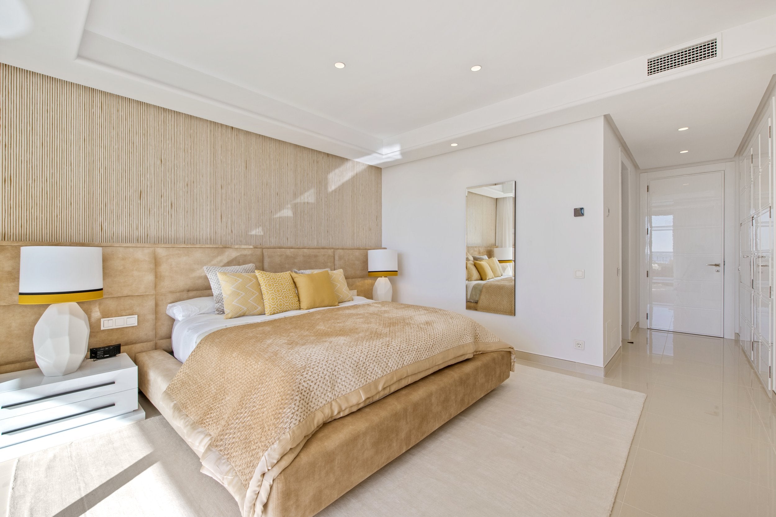 beautiful yellow modern bedroom interior design with long headboard and beige rug, bedside table with elegant table lamps available in bel air, malaga, marbella, costa del sol, benahavis.