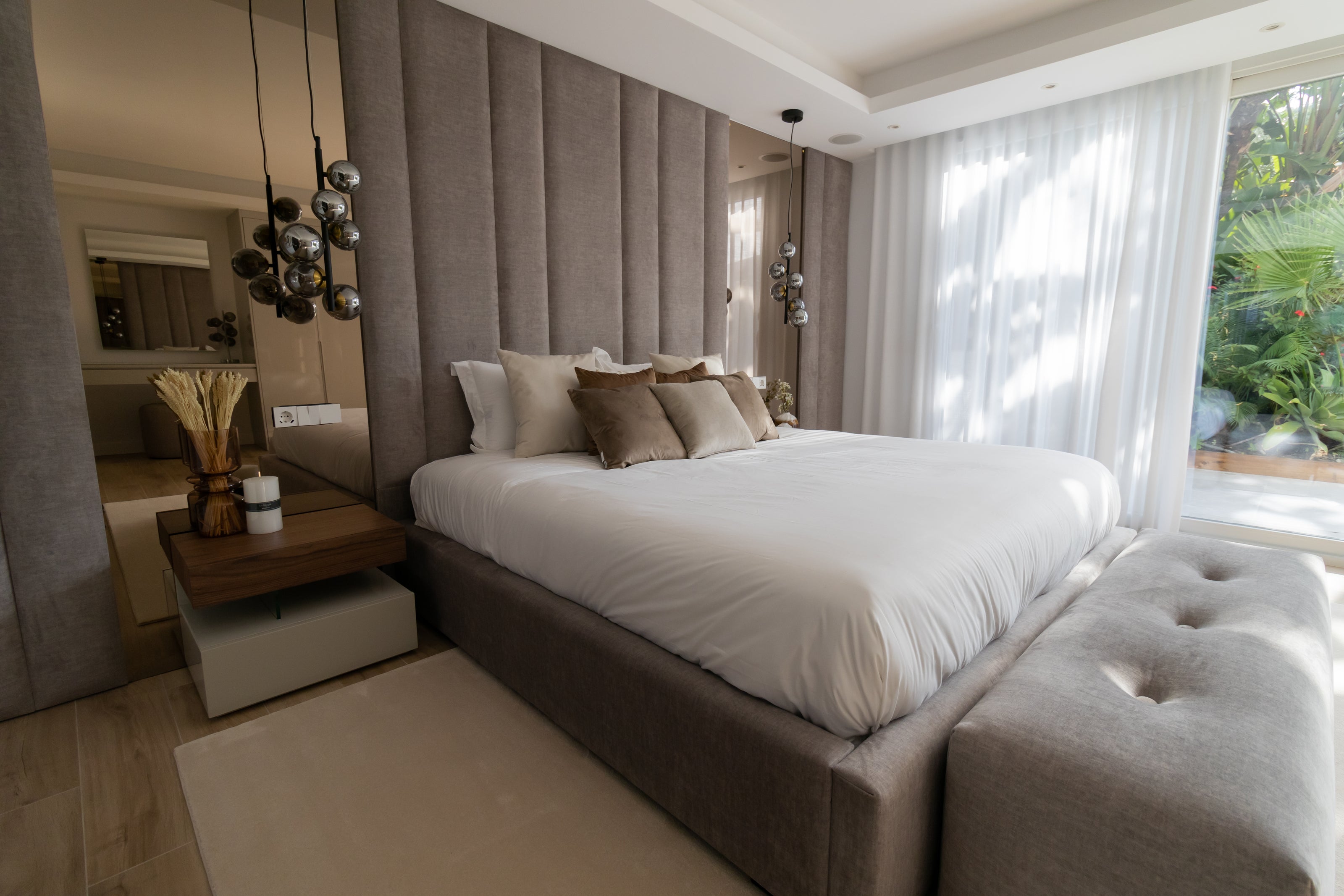 Elegant contemporary interior design, home design for bedroom with bronze mirror, tall headboard, bed, bedside table, ottoman, rug and ceiling lamp available in casares, marbella, malaga, costa del sol.